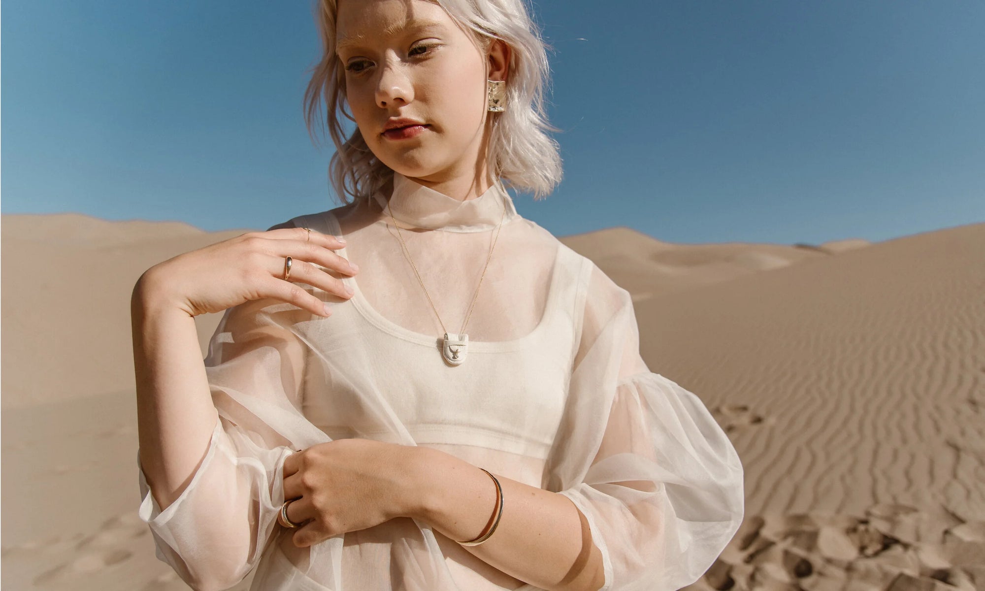 Model Aleah Hyvonen wears the Plane Earrings, Brilliant Diamond Talisman Pouch Necklace, Portal Bracelet, Rollo Band, Portal Ring, and Circle Shape Ring. All sustainably handmade in recycled 14k gold using traditional lost-wax casting techniques.