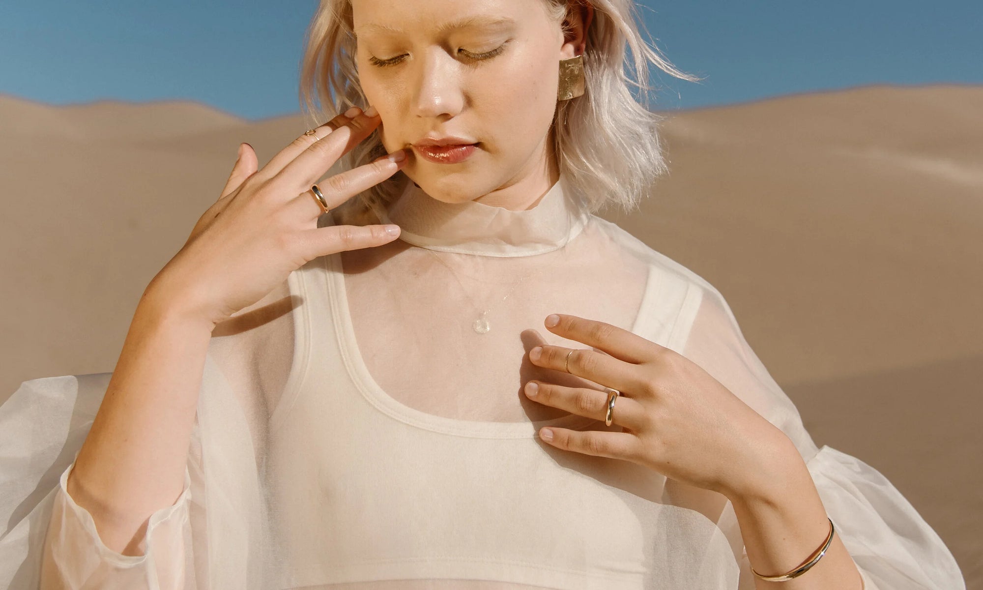 Model Aleah Hyvonen wears the Plane Earrings, Michael Amulet Necklace, Whisper Chain, Portal Bracelet, Circle Shape Ring, Portal Ring, Goldyn Hammered Stacking Band, and Rollo Band. All sustainably handmade in recycled 14k gold using traditional lost-wax casting techniques.