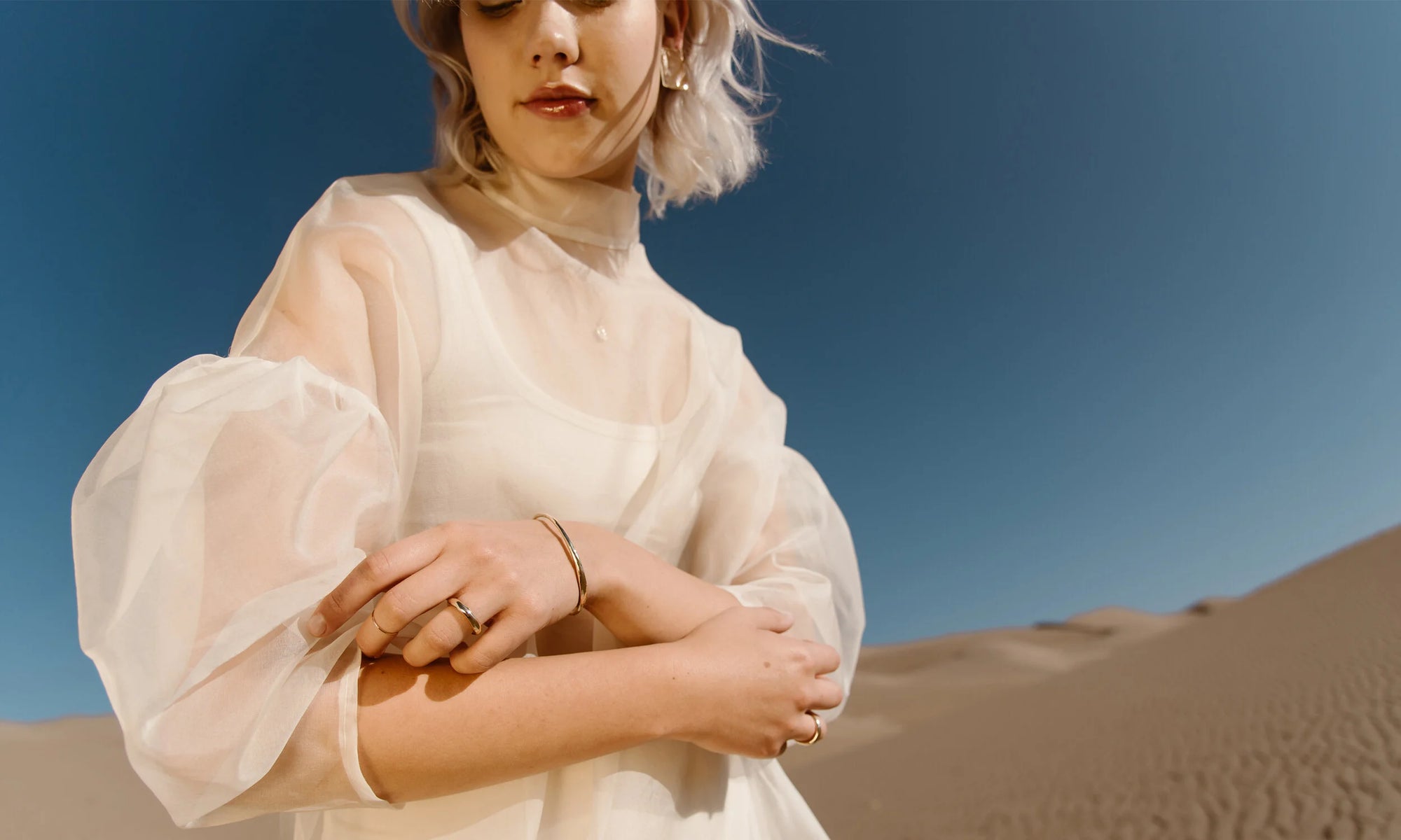 Model Aleah Hyvonen wears the Plane Earrings, Michael Amulet Necklace, Whisper Chain, Portal Bracelet, Goldyn Hammered Stacking Ring, Rollo Band, and Portal Ring. All sustainably handmade in recycled 14k gold using traditional lost-wax casting techniques.