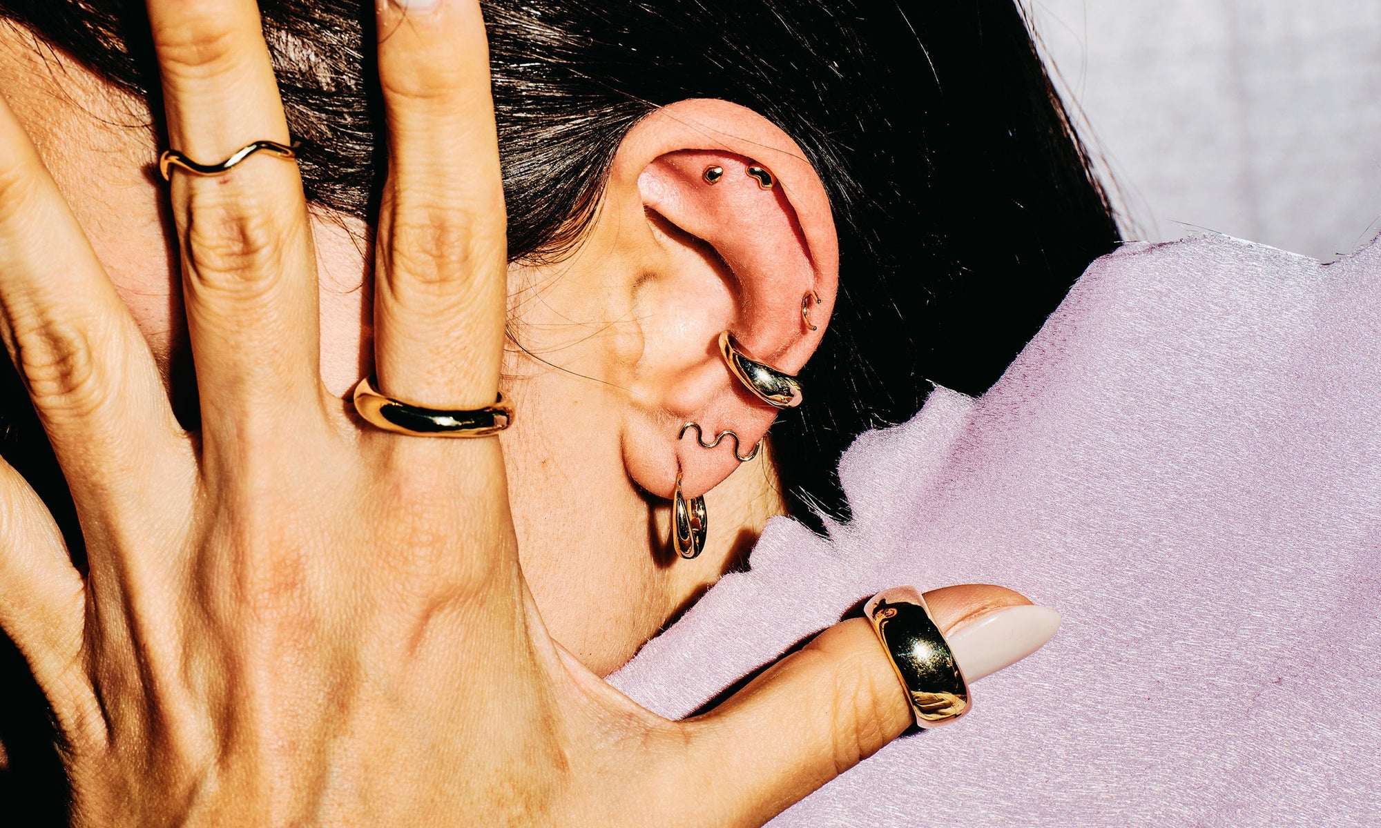 Model Vanessa Luka wears, from left: the Wave Theory Ring, Rollo Band, and Conjunct Cigar Band, along with the Aphrodite Hugs, Wave Stud, Delphi Ear Cuff, Outward Arc Stud, and Mini Orb Studs. All hand-sculpted and sustainably made using recycled 14k gold.