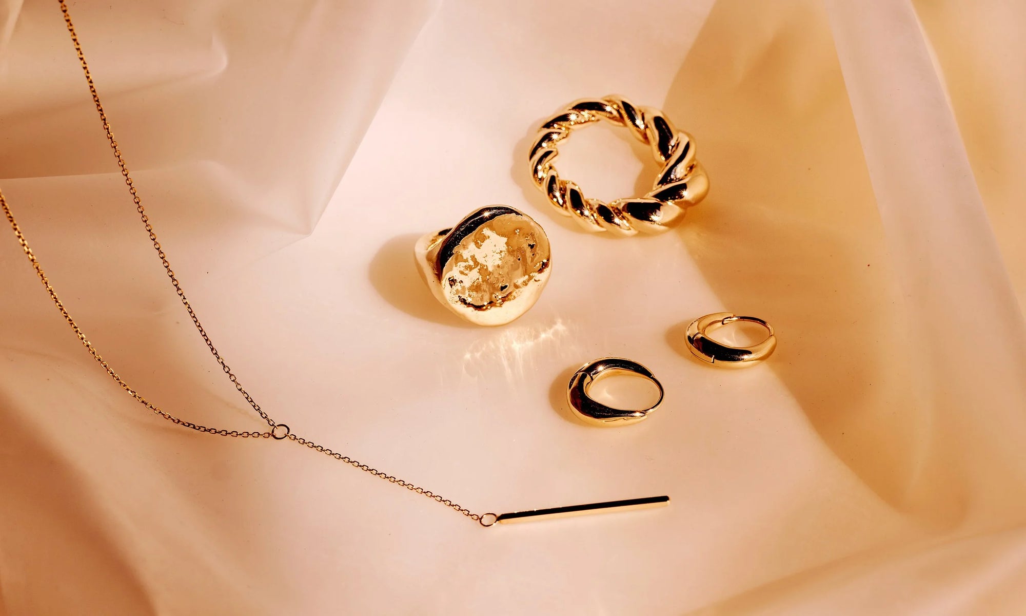 Clockwise from top: the Helix Ring, Aphrodite Hugs, Linear Y Necklace and Ra Pinky Signet. All sustainably handmade in recycled 14k gold.