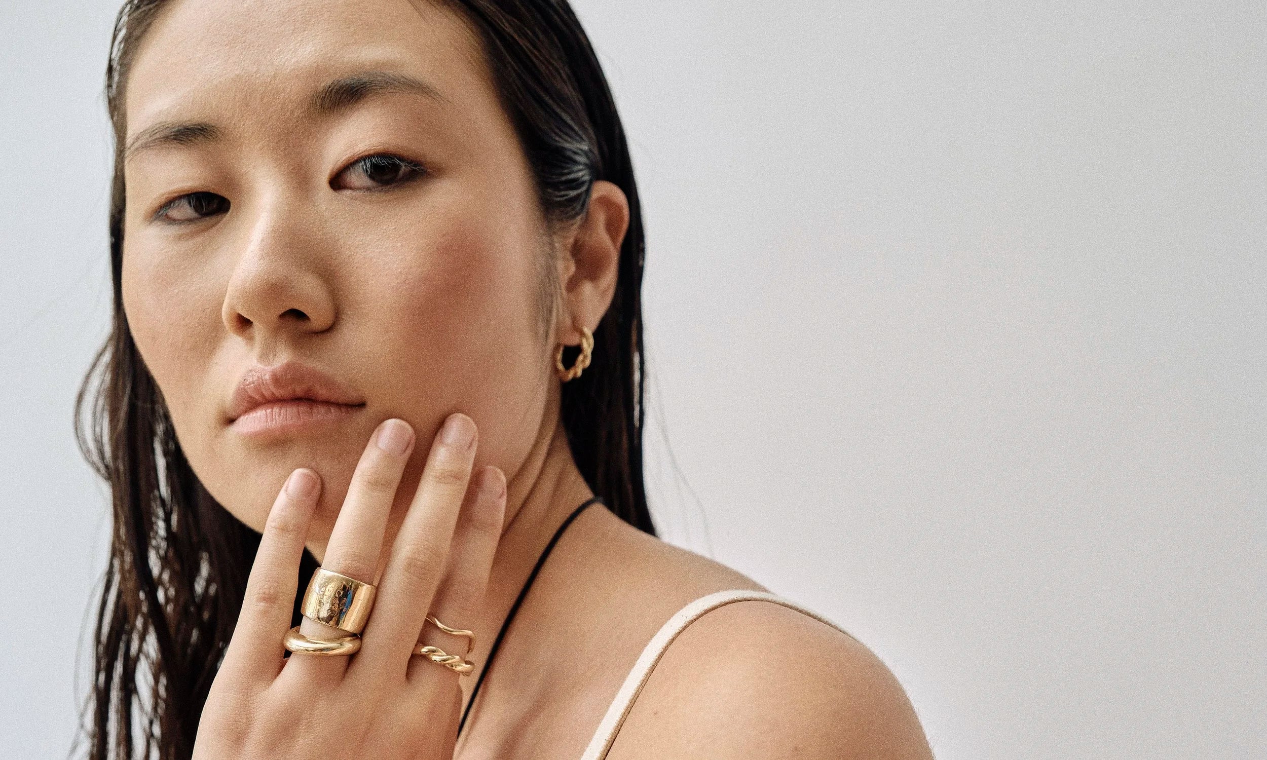 Model Rachel wears the Demeter Cigar Band, Persephone Ring, Wave Theory Ring, Helix Band, and Helix Hoop Earring. All sustainably handmade in solid recycled 14k gold by Talisman Fine Jewelry.