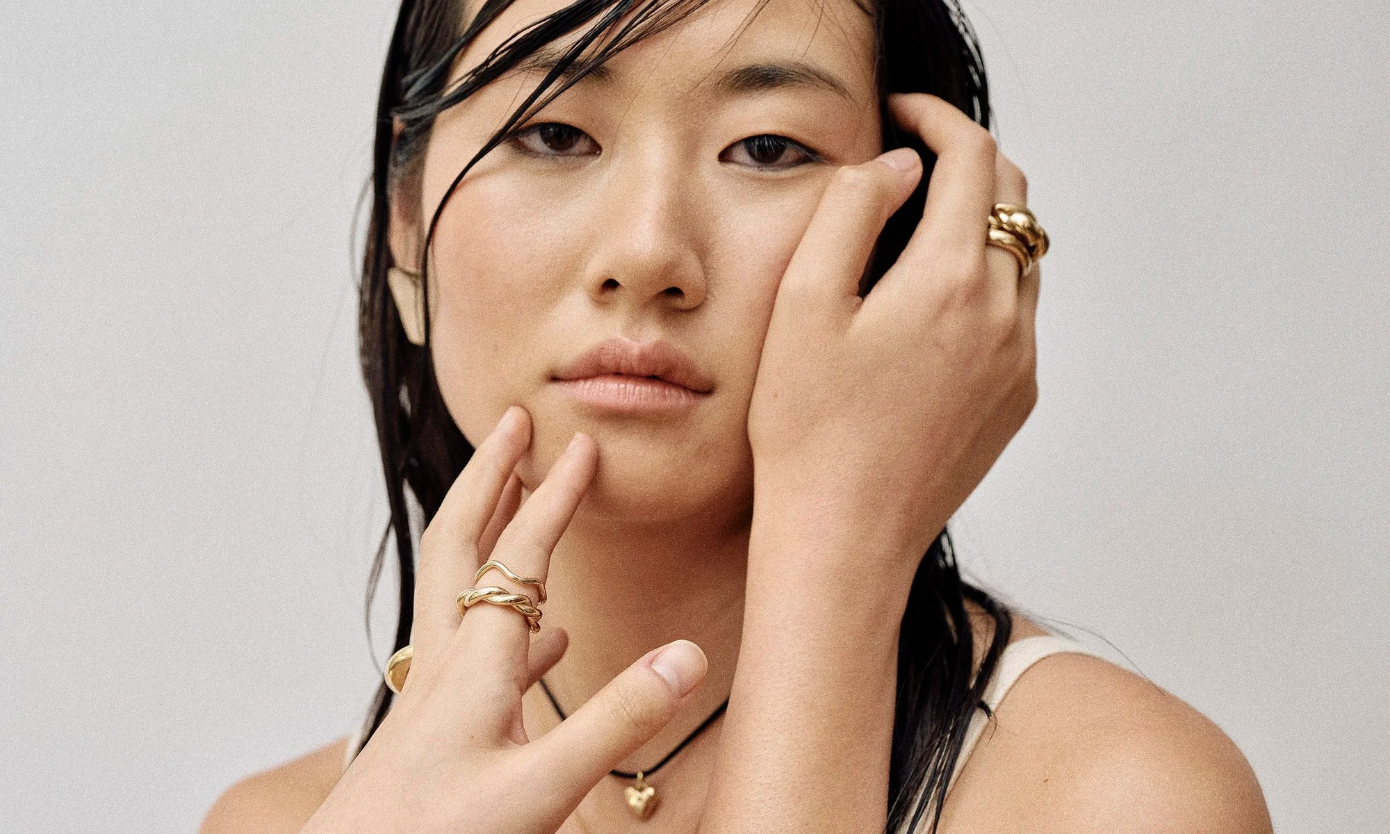 Model Rachel wears the Plane Earrings, Zoe's Heart Necklace on a silk cord, Portal Ring, Helix Dome Ring, and Rollo Band, as well as the Wave Theory Ring, Helix Band, and Persephone Ring. All sustainably handmade in recycled 14k gold by Talisman Fine Jewelry.