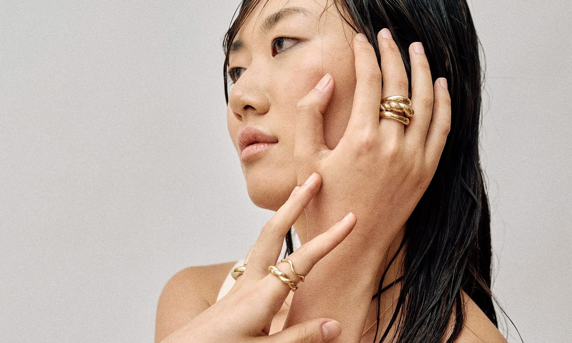 Model Rachel wears the Portal Ring, Helix Dome Ring, and Rollo Band, as well as the Wave Theory Ring, Helix Band, and Persephone Ring. All sustainably handmade in recycled 14k gold by Talisman Fine Jewelry.