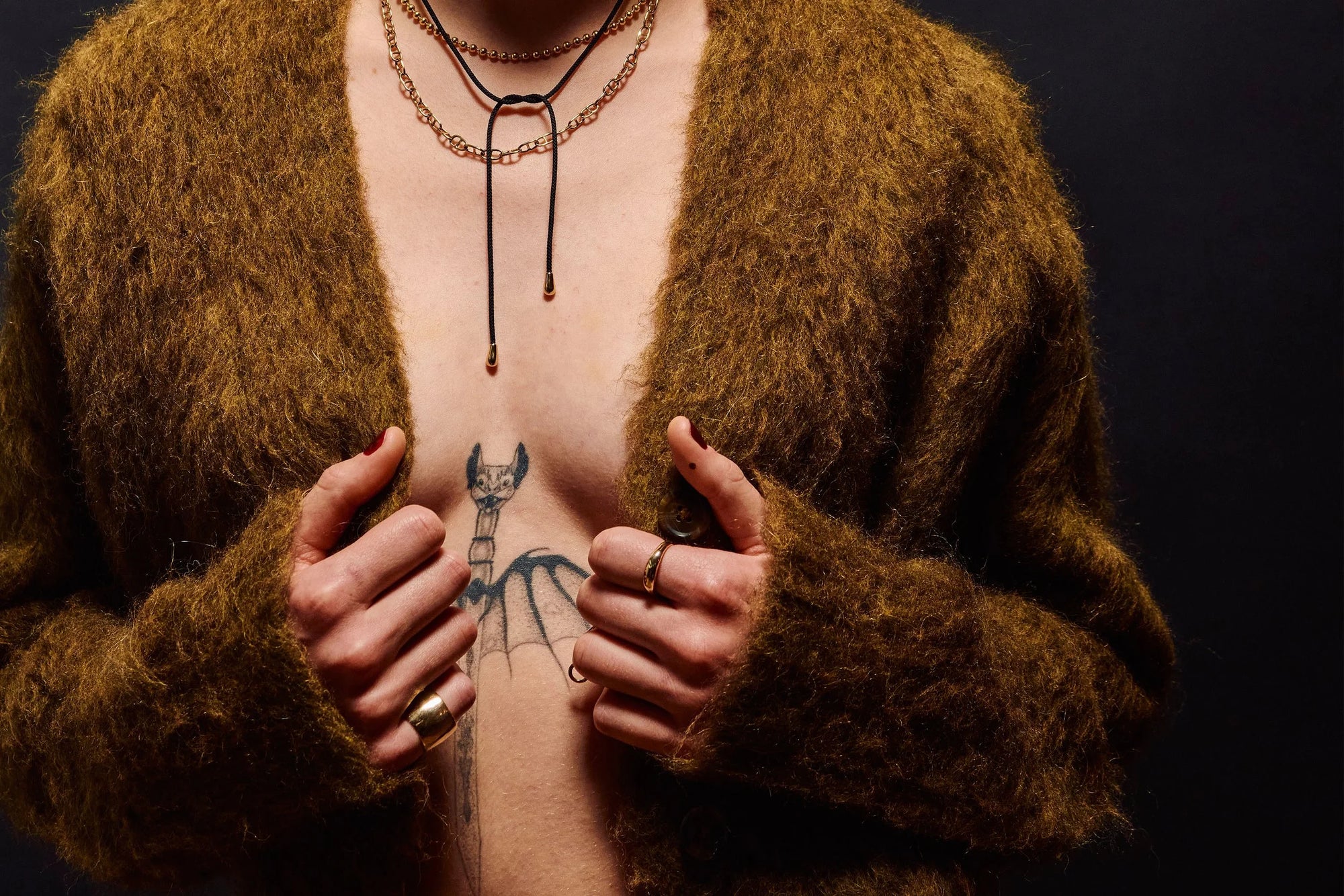 Rae wears layered necklaces including the solid 14k Gold Galaxy Chain, handmade Anchored Handmade Chain, and reversible Drip Silk Cord Choker. With Demeter Cigar Band and Portal Ring on their hands.