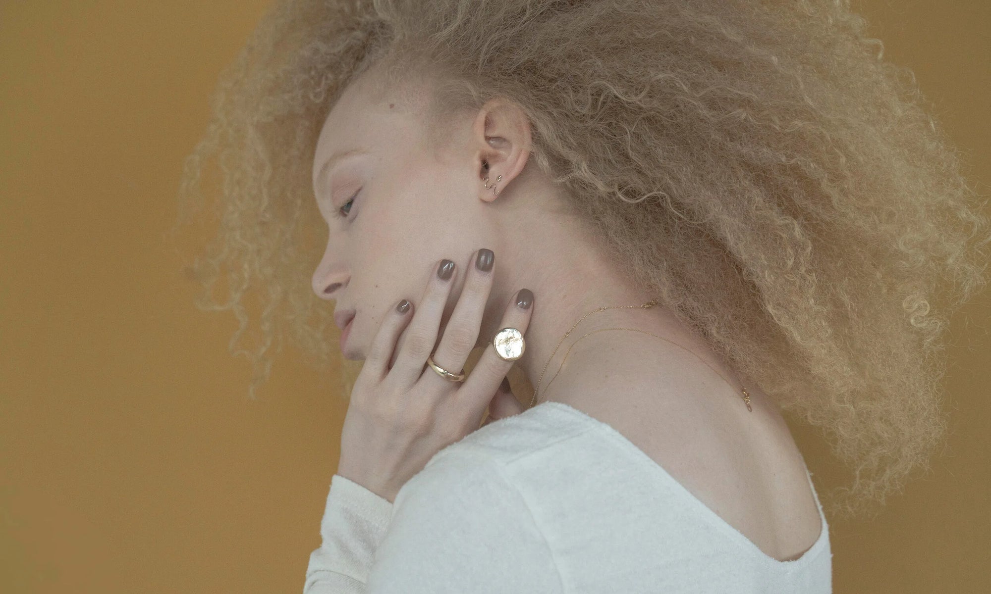 Model Nyasia Wyani wears the Rollo Band, Ra Pinky Signet as a midi ring, layered Whisper Chain and Michael Amulet Necklace, along with the Wave Stud and Mini Orb Stud. All sustainably handmade in recycled 14k gold.