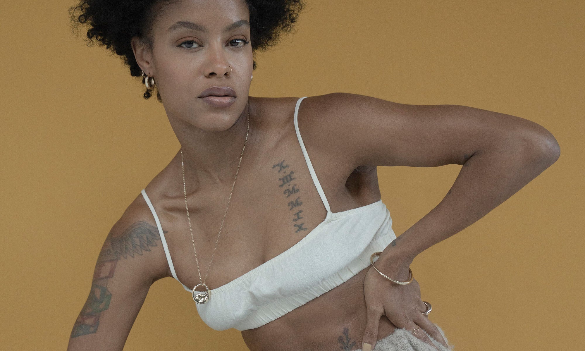 Model Alicia Myers wears the Talisman Fine Jewelry Alchemy Collection. Clockwise from bottom left: The Yin Yang Necklace, Rollo Hoops, Moon Stud, Portal Bracelet, Persephone Ring, and Circle Shape Ring. All sustainably handmade in recycled 14k gold, using traditional lost-wax casting techniques.