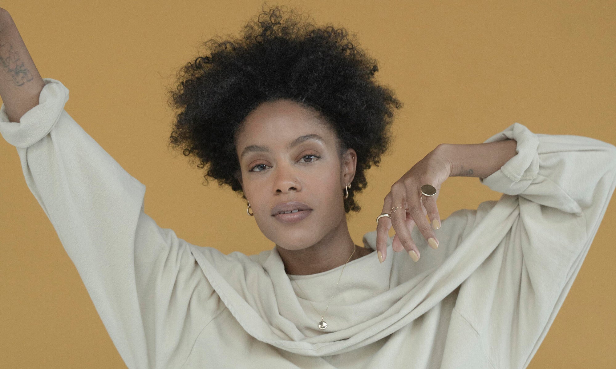 Model Alicia Myers wears the Ra Pinky Signet, Circle Shape Ring, Rollo Band, Michael Amulet Necklace, Aphrodite Hugs, Peace Sign Stud, and Mini Orb Stud. All sustainably handmade using traditional lost-wax casting techniques, in recycled 14k gold.