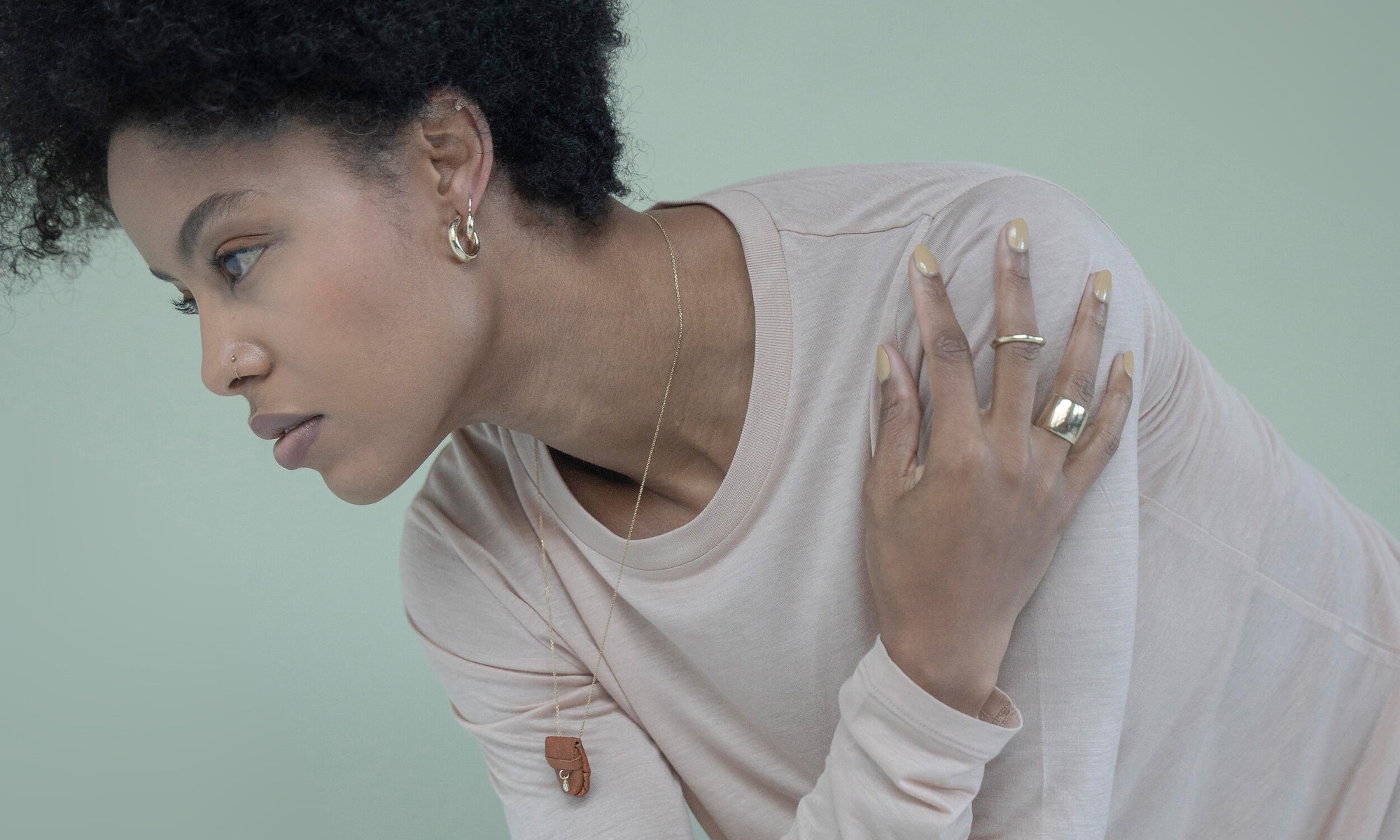 Model Alicia Myers wears the Rose Cut Diamond Talisman Pouch Necklace, Petite Rollo Band, Demeter Cigar Band, Rollo Hoops, Aphrodite Hugs, and Mini Rainbow Studs. All sustainably handmade in recycled 14k gold, using traditional lost wax casting techniques.