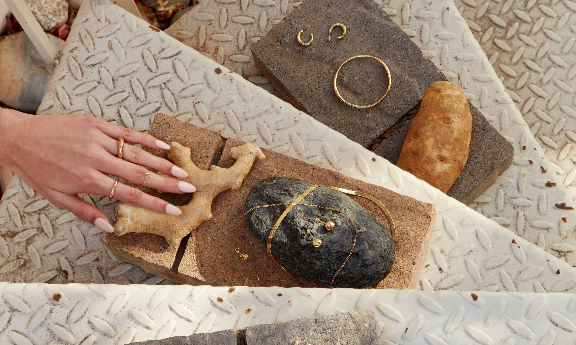 Grabbing for it, Alianna Martinez wears the Persephone Ring, Petite Rollo Band, and Triangle Shape Ring. On bricks, from top: Rollo Hoops, Portal Bracelet, Flow Chain, Rose Cut Diamond Drop Necklace, and Central Sun Earrings.