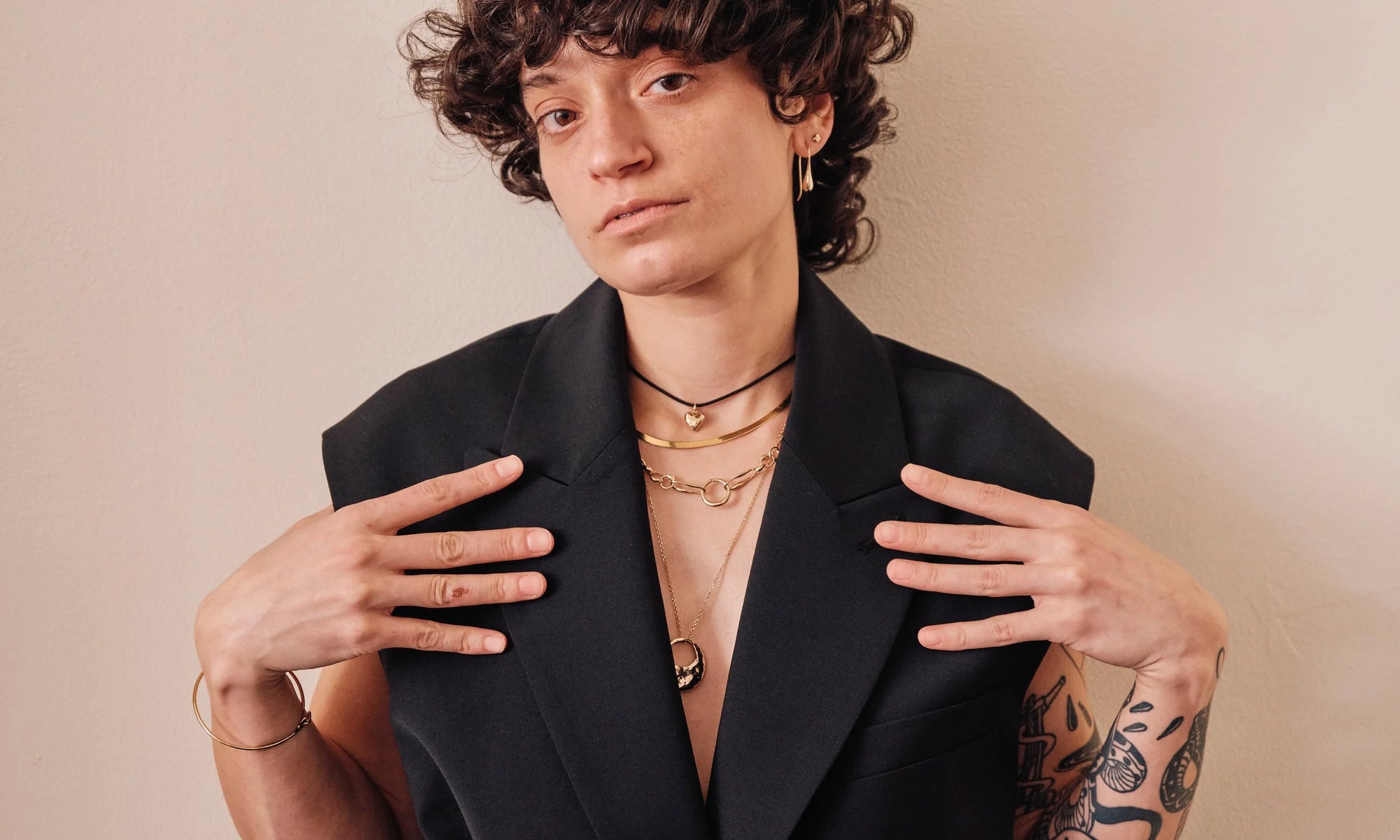 Model Erika Rodriguez wears from top: Diamond Mini Orb Stud, Sanguine Drop Earrings, Zoe's Heart Necklace, Flow Chain, Metanoia Handmade Chain, Yin Yang Necklace, and the Orbit Bracelet. All sculpted and handmade in solid, recycled 14k gold.