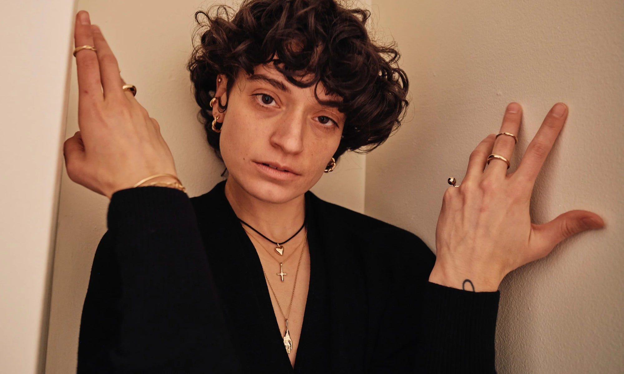 Model Erika Rodriguez wears the Helix Hoops, Ouroboros Ring, Zoe's Heart Necklace on silk cord, Petite Christ Consciousness Necklace, and Held Necklace. All sustainably handmade in recycled 14k gold.