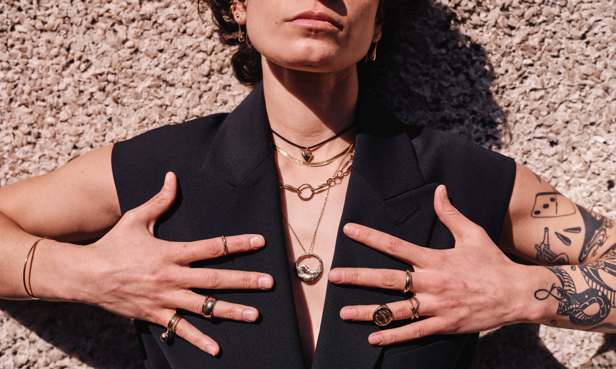 Erika wears, from left: Orbit Bracelet, Central Sun Ring, Infinite Ring Stack, Portal Ring paired with Conjunct Cigar Band, Petite Helix Band, Zoe's Heart Necklace on silk cord, Flow Chain, Metanoia Handmade Chain, Yin Yang Necklace, Ra Pinky Signet Ring, Ouroboros Ring, Shapeshifter Ring, and Rollo Band, along with the Sanguine Drop Earrings. All handmade in recycled 14k gold.